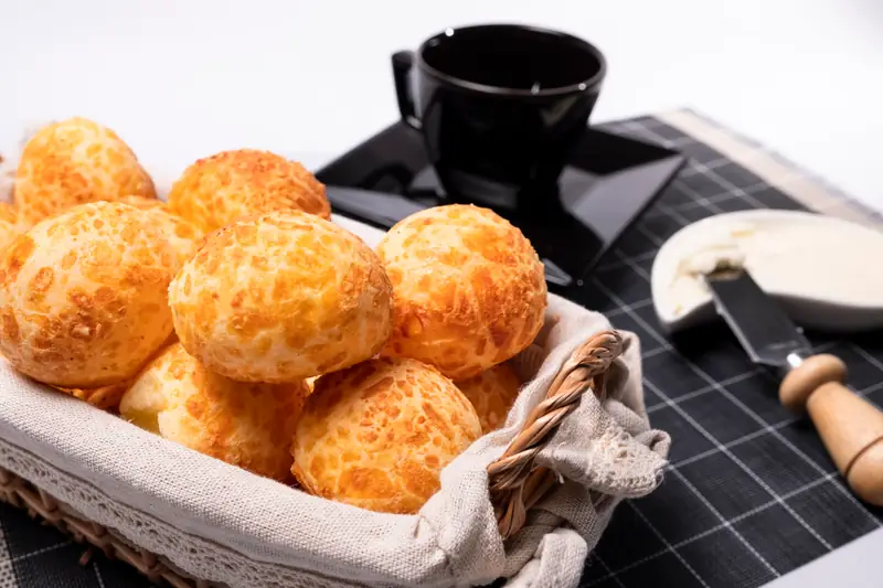 Cesta de pães de queijo dourados com xícara de café ao fundo