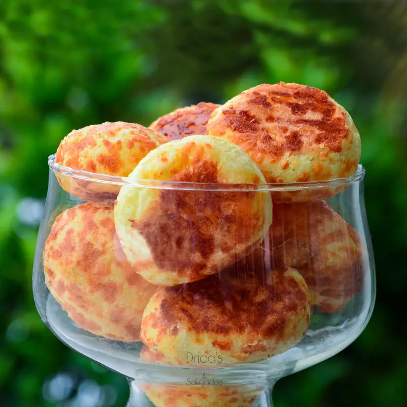 Pães de queijo dourados em taça de vidro sobre fundo verde